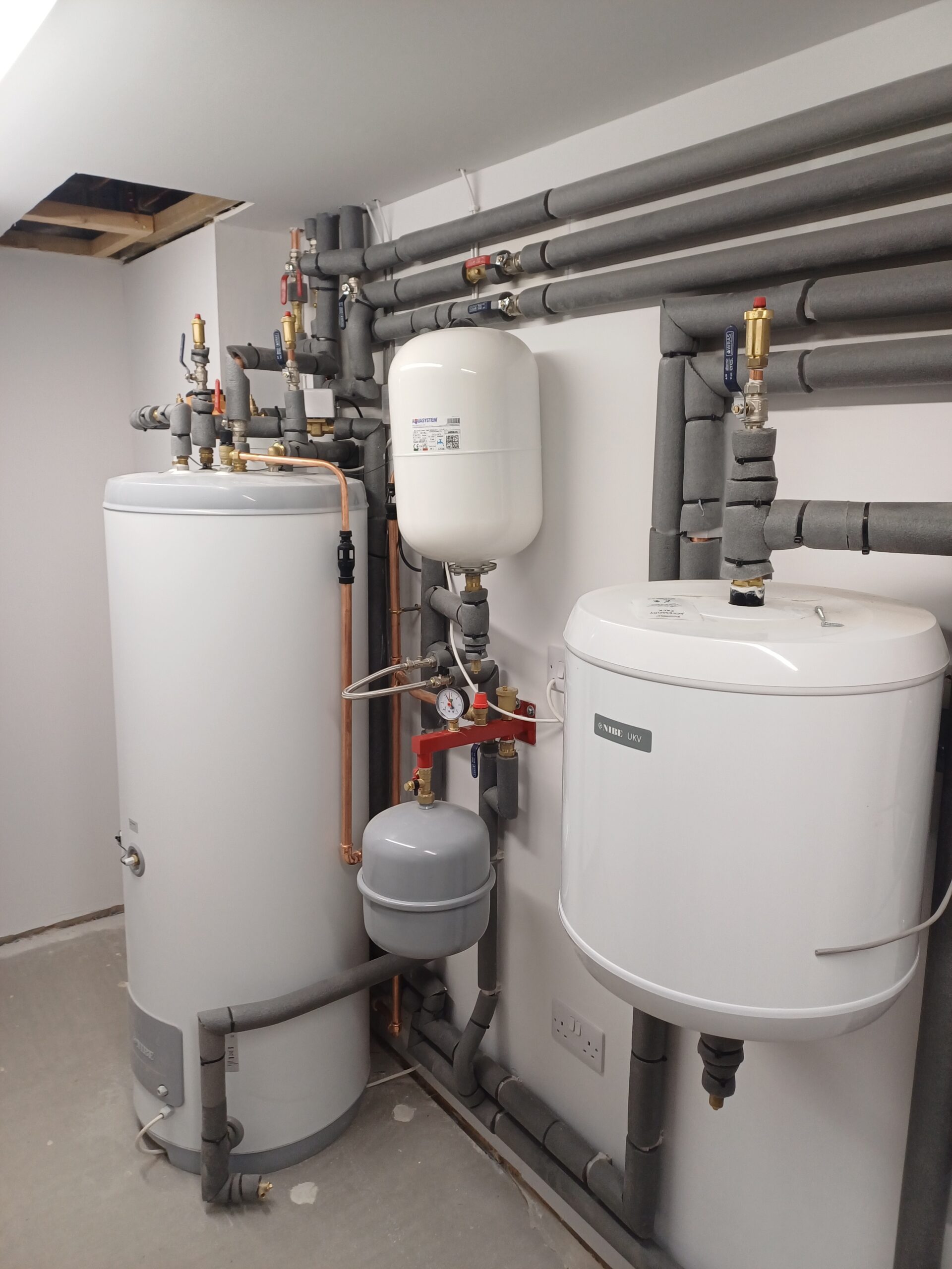 Hot water cylinder and expansion vessel system installed in a utility room, featuring insulated pipework and pressure controls