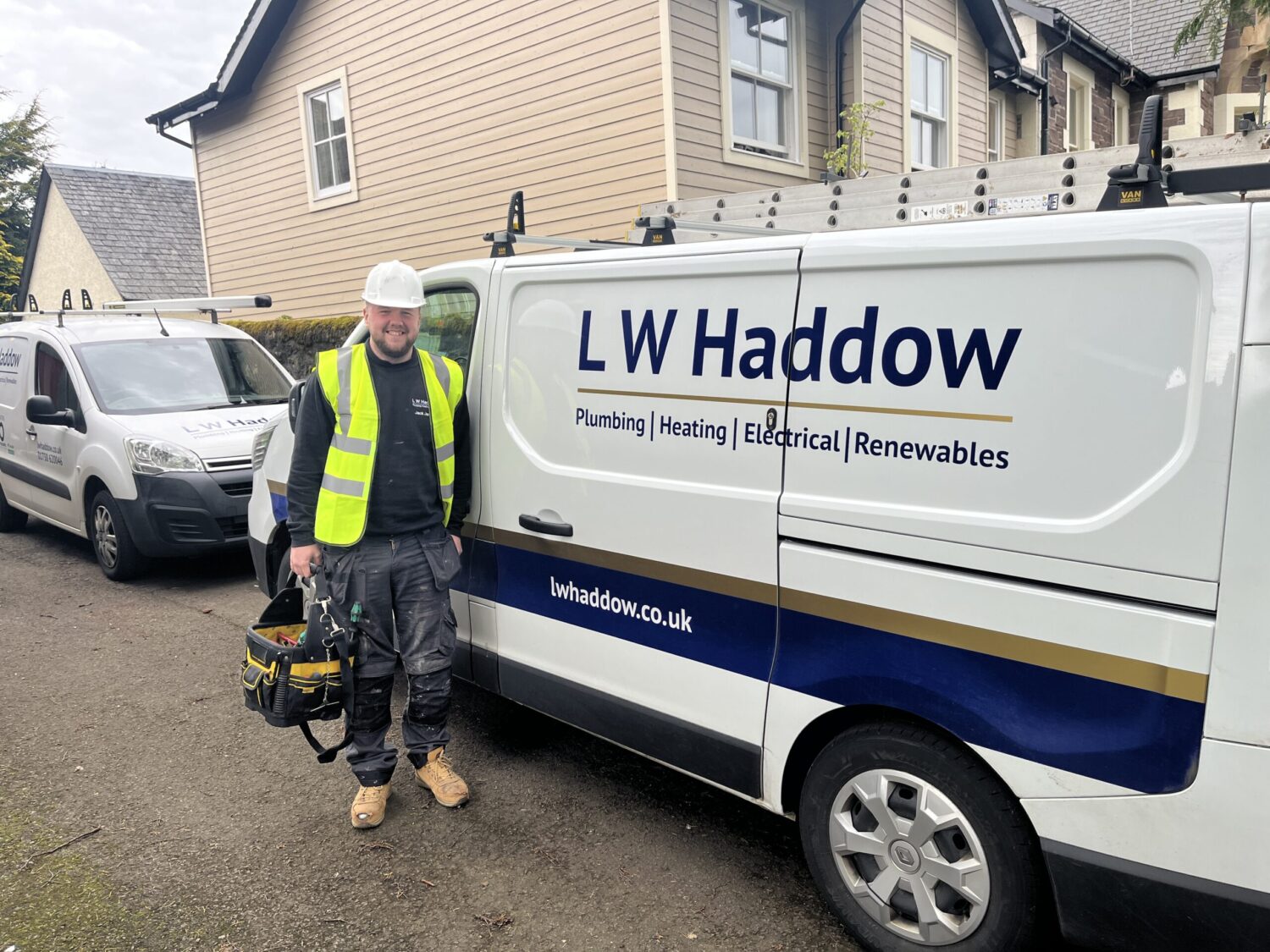 An LW Haddow heating technician wearing a hard hat and high visibility vest at a commercial site holding a tool bag ready to carry out professional heating services