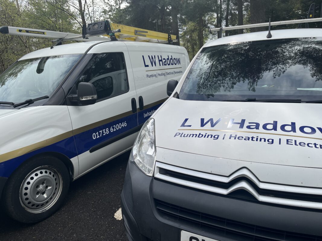 LW Haddow Plumbing and Heating vans, showcasing company logos and contact details for plumbing, heating, electrical, and renewables.